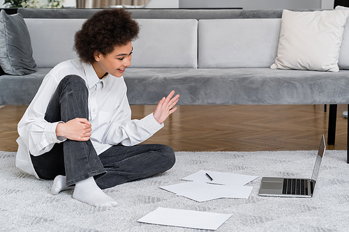 happy african american woman having video chat on laptop while sitting near velvet grey sofa