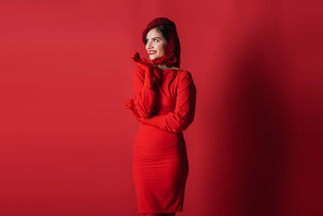 happy and elegant woman in beret and dress posing on red