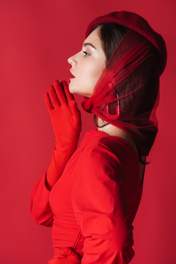 side view of elegant young woman in beret and dress isolated on red