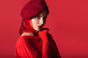 elegant young woman in beret and glove looking at camera isolated on red