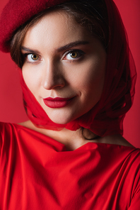 close up of elegant young woman in beret looking at camera isolated on red