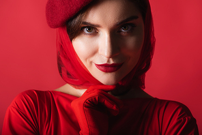 cheerful young woman in glove, headscarf and beret isolated on red