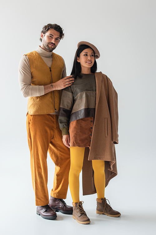 trendy man looking at camera near asian woman in beret and yellow tights on grey