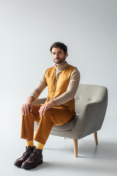 full length view of man in yellow vest and trousers sitting in armchair on grey