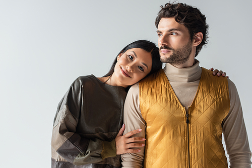 happy asian woman leaning on brunette man in yellow vest isolated on grey