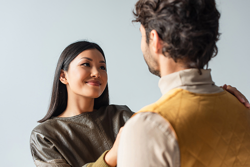 pretty asian woman smiling at blurred man isolated on grey