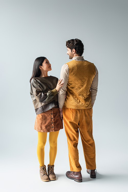 back view of man in yellow vest and trousers near smiling asian woman on grey