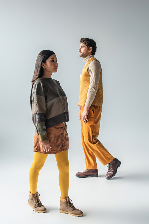 full length view of asian woman and brunette man in stylish clothes walking on grey