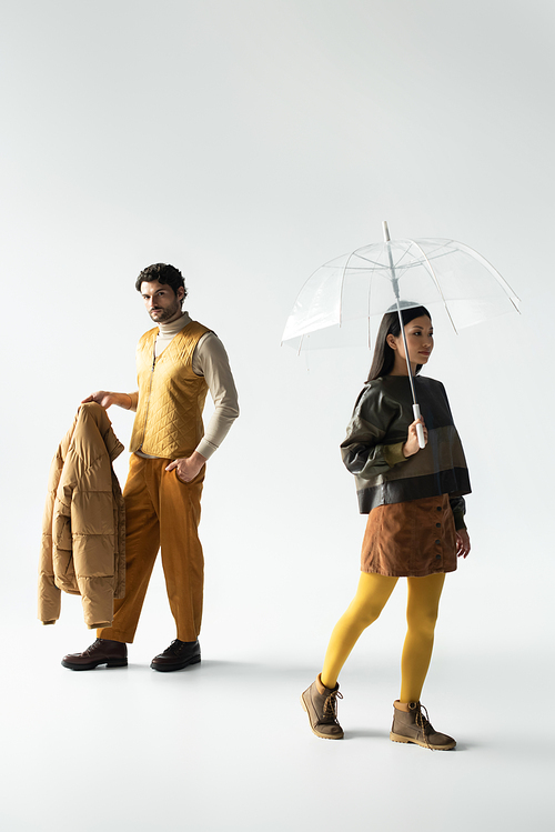 man with puffer jacket and asian woman with transparent umbrella walking on grey