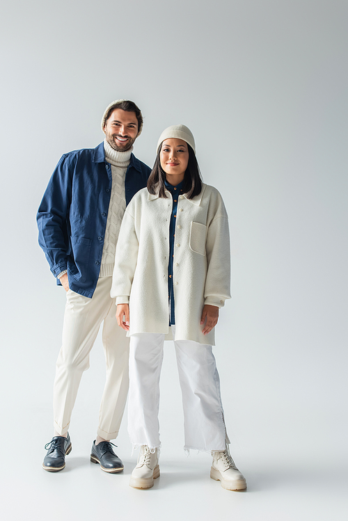 full length view of interracial couple in trendy white and blue clothes on grey background