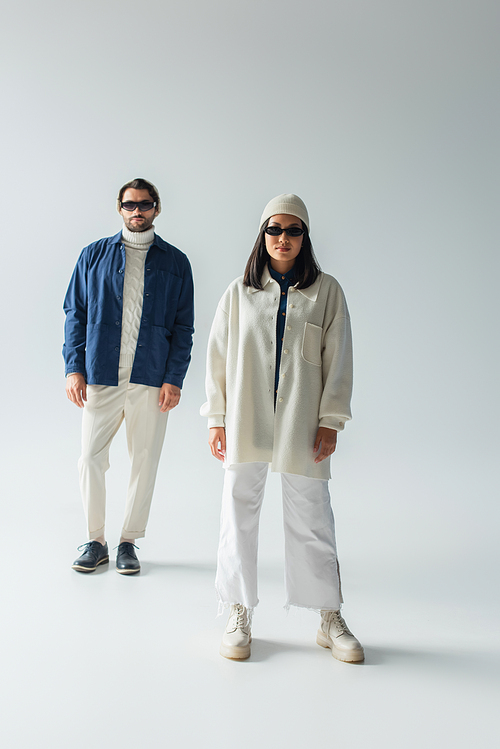 full length view of interracial couple in white and blue clothes standing on grey