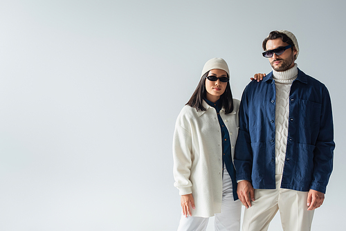 trendy interracial couple in dark sunglasses looking at camera isolated on grey