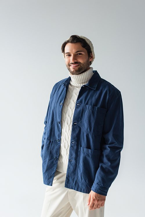 happy man in blue jacket and white knitted sweater smiling at camera isolated on grey