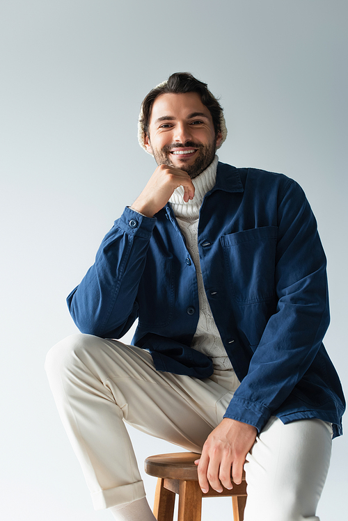 cheerful man in white trousers and blue jacket looking at camera isolated on grey