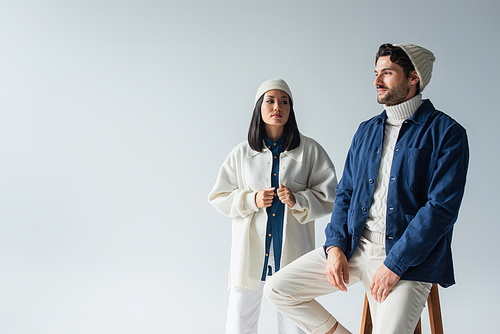 man in blue jacket sitting on high stool near stylish asian woman isolated on grey