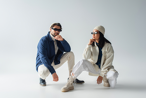 interracial couple in trendy clothes and dark sunglasses posing on grey