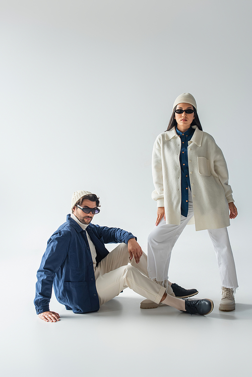 asian woman in white clothes and dark sunglasses posing near man sitting on grey