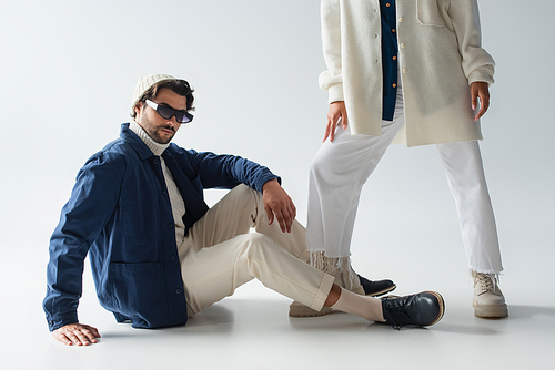 stylish man in blue jacket and dark sunglasses sitting near woman on grey