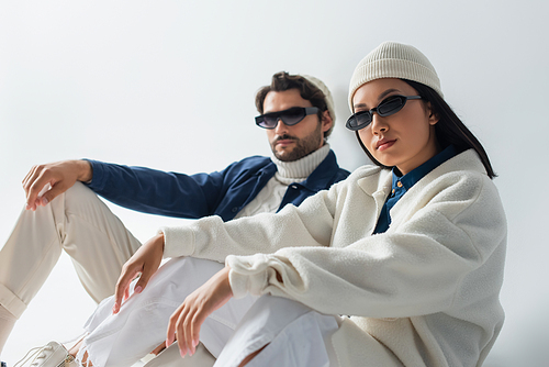 trendy asian woman in dark sunglasses sitting near blurred man on grey