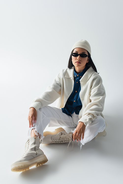 asian woman in white clothes and dark sunglasses looking at camera while sitting on grey