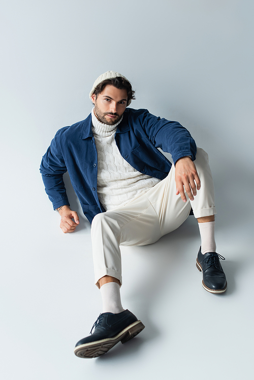 high angle view of man in white trousers and blue jacket looking at camera while sitting on grey