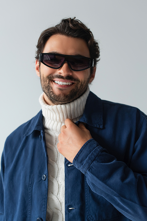 smiling man in blue jacket and dark sunglasses isolated on grey