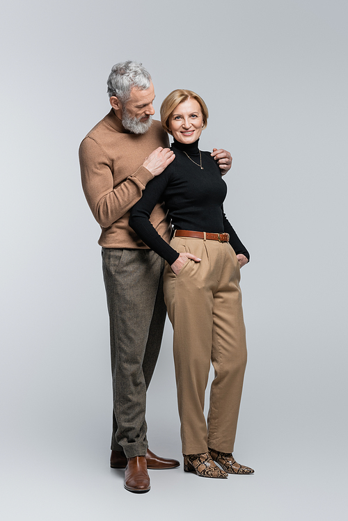 Stylish mature man hugging wife on grey background