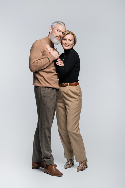 Stylish mature couple looking at camera and hugging on grey background