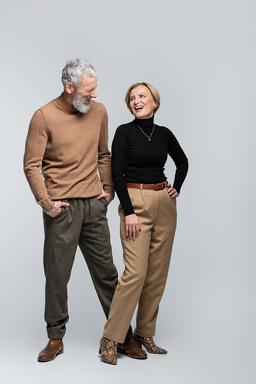 Cheerful stylish woman looking at mature husband on grey background