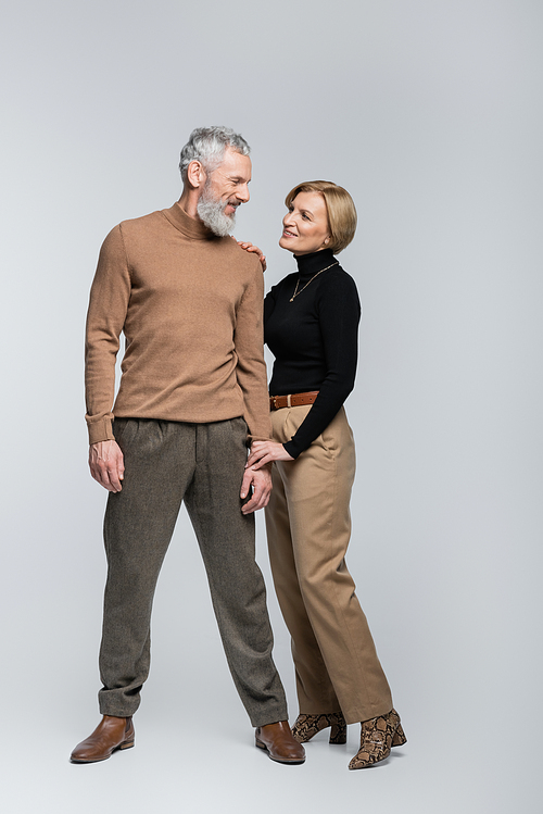 Positive mature woman holding hand of stylish man on grey background