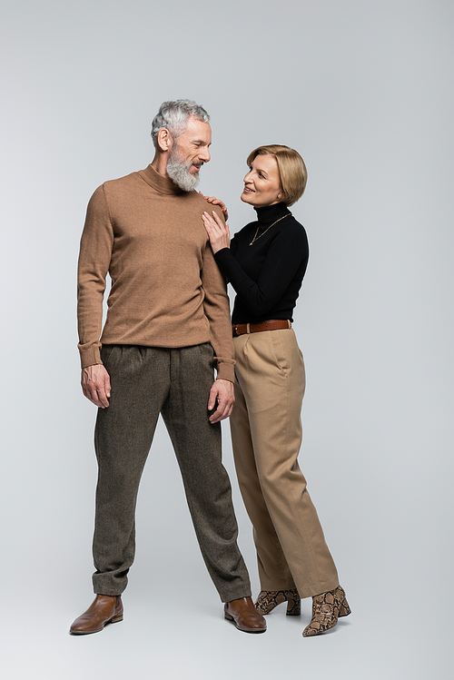 Blonde woman touching stylish mature husband on grey background