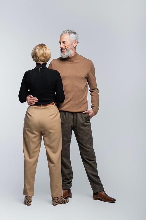 Smiling mature man hugging blonde wife on grey background