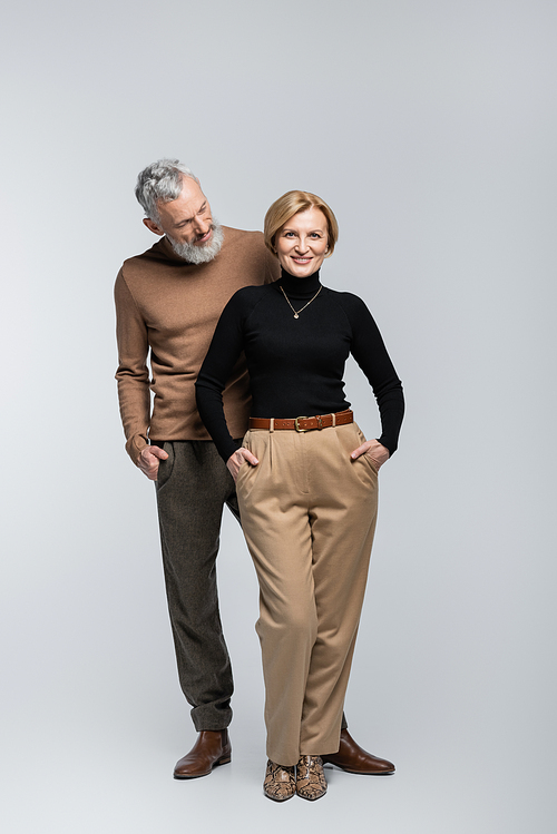 Bearded stylish man looking at blonde wife smiling at camera on grey background