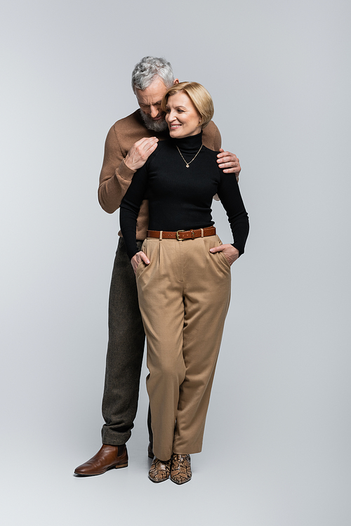 Stylish bearded man hugging blonde wife in turtleneck on grey background