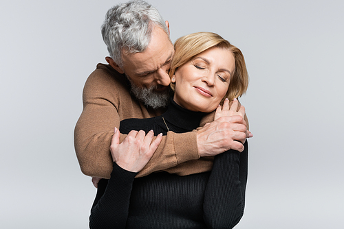 Grey haired man hugging wife with closed eyes isolated on grey