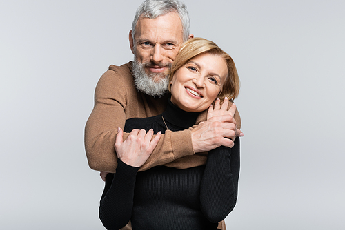 Portrait of mature man hugging positive wife isolated on grey