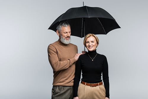 Stylish man holding umbrella above smiling wife isolated on grey