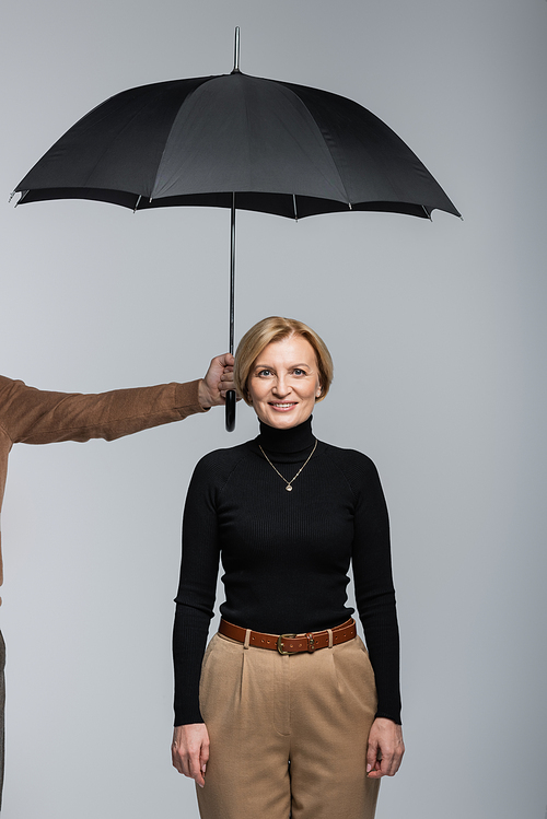 Man holding umbrella above smiling wife isolated on grey