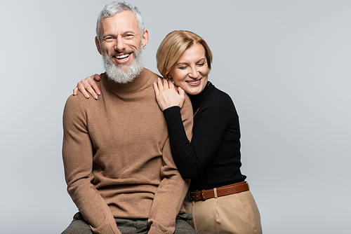 Blonde woman in turtleneck hugging mature husband isolated on grey