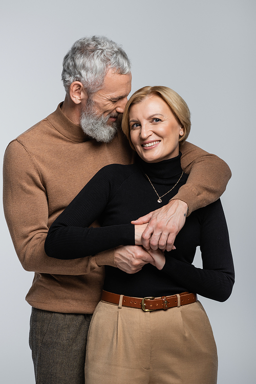 Grey haired man in turtleneck embracing blonde wife isolated on grey