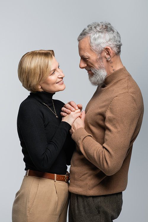 Cheerful mature and stylish couple holding hands isolated on grey