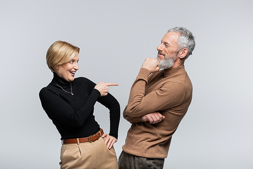 Positive mature woman pointing at stylish husband isolated on grey