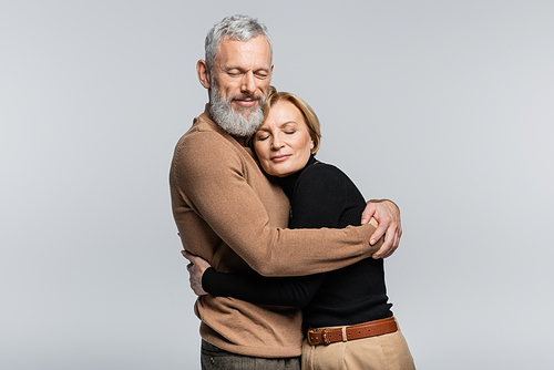 Bearded grey haired man hugging wife with closed eyes isolated on grey