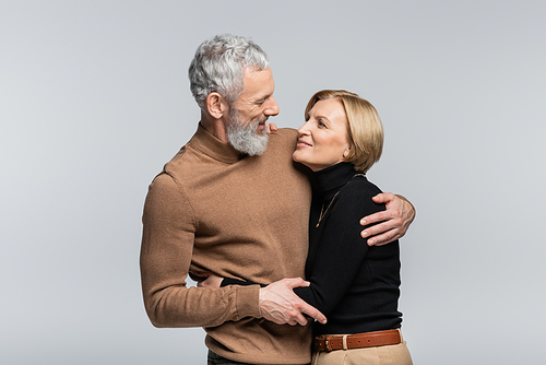 Positive man hugging middle aged wife in turtleneck isolated on grey