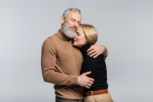 Mature man closing eyes and hugging stylish wife isolated on grey