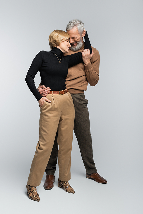 Full length of cheerful mature couple hugging and posing on grey background