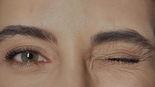 close up view of woman with hazel eyes and mascara on eyelashes winking while looking at camera