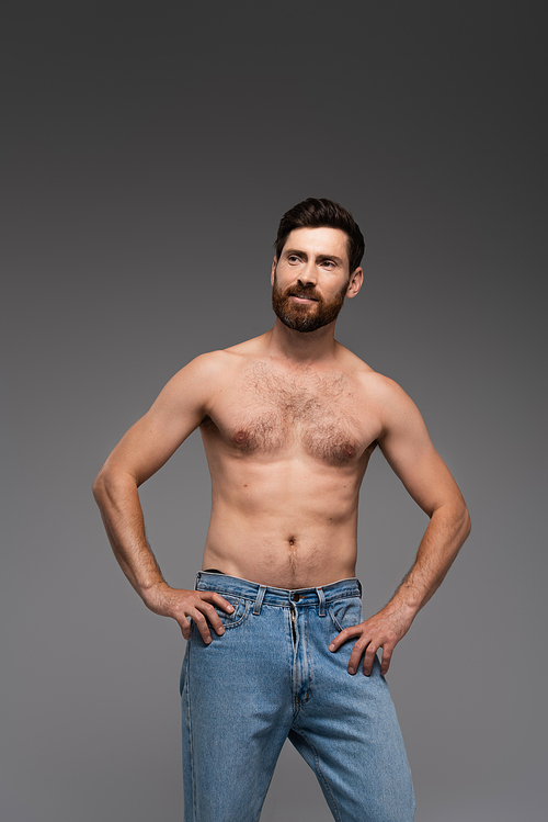 shirtless man with beard posing in denim jeans and smiling isolated on grey