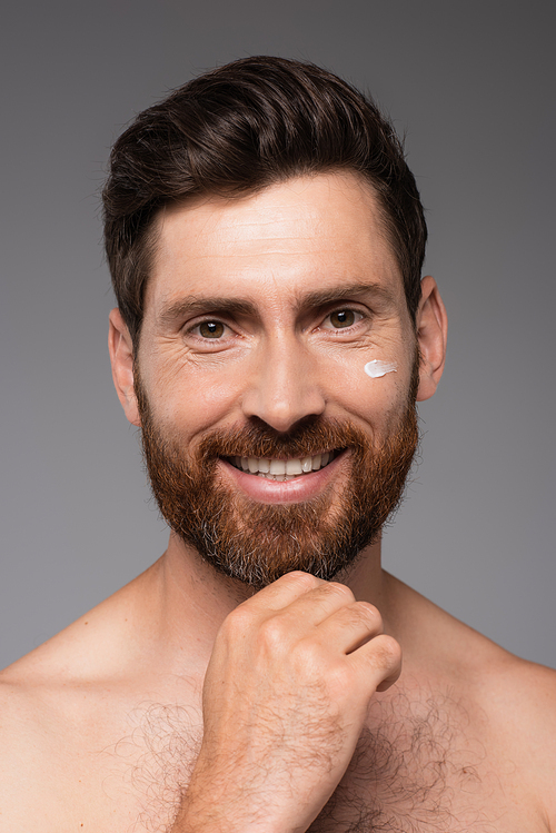portrait of smiling bearded man with cream on face looking at camera isolated on grey