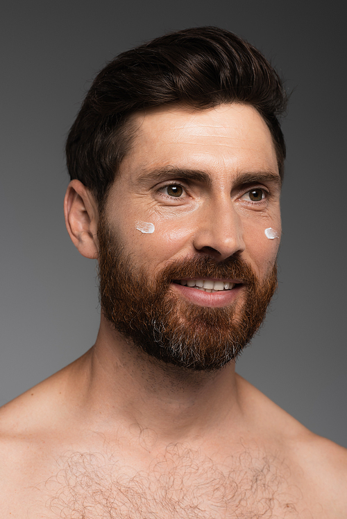 portrait of bearded man with cream on face smiling isolated on grey